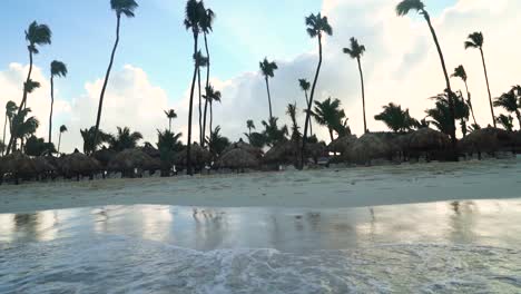 caribbean sea is reaching the beach with pulms and sun beds. waves move back and forward to the beach. view from the sea