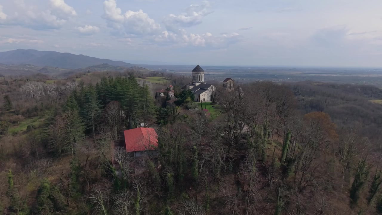 Aerial reveal of Martvili Monastery rising above the treetops, showcasing its historic architecture within the serene natural surroundings of Georgia.