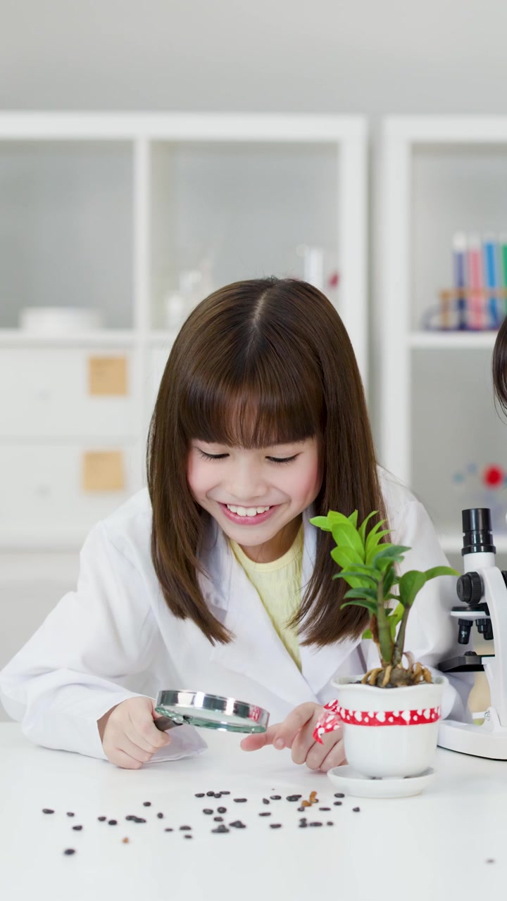 Young student in white lab coat uses magnifying glass to study plant and seeds.