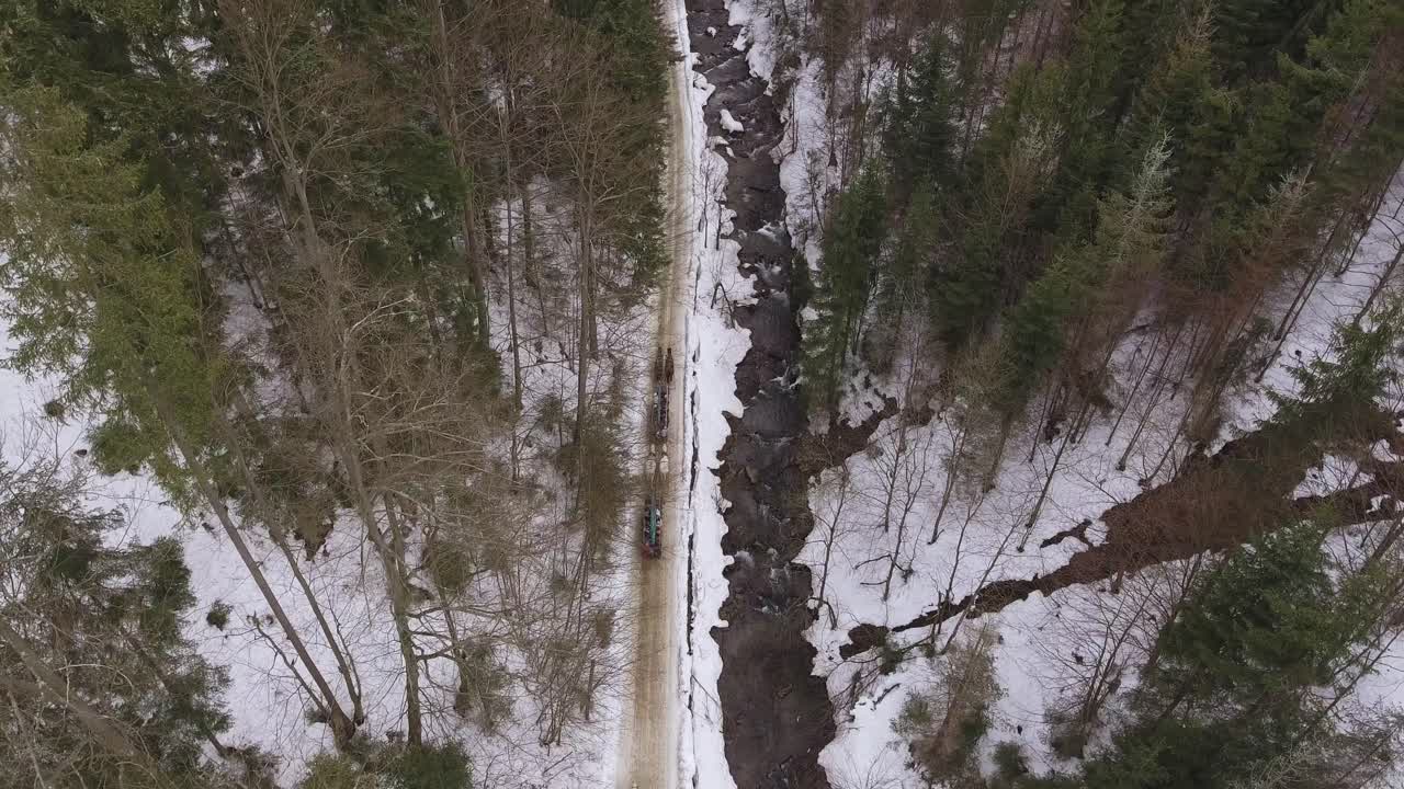 Three horse teams ride a narrow mountain valley next to a river during late winter