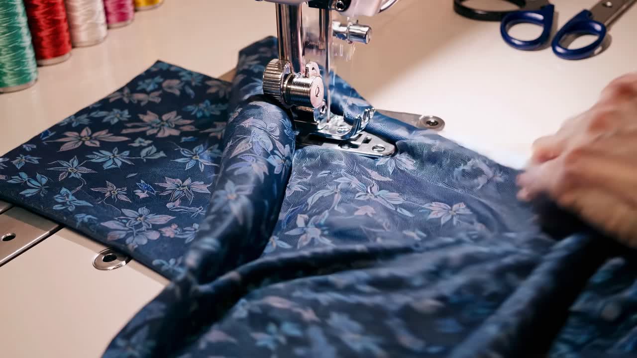 Close-up video of hands sewing floral fabric on a machine, showcasing intricate patterns