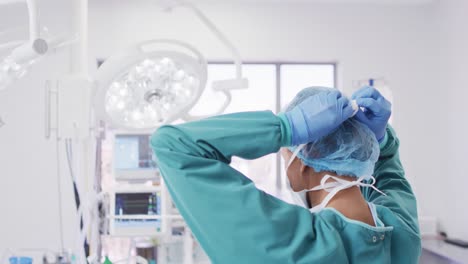 Video-Einer-Gemischtrassigen-Chirurgin-In-Handschuhen,-Die-Im-Operationssaal-Eine-Gesichtsmaske-Bindet,-Mit-Kopierraum