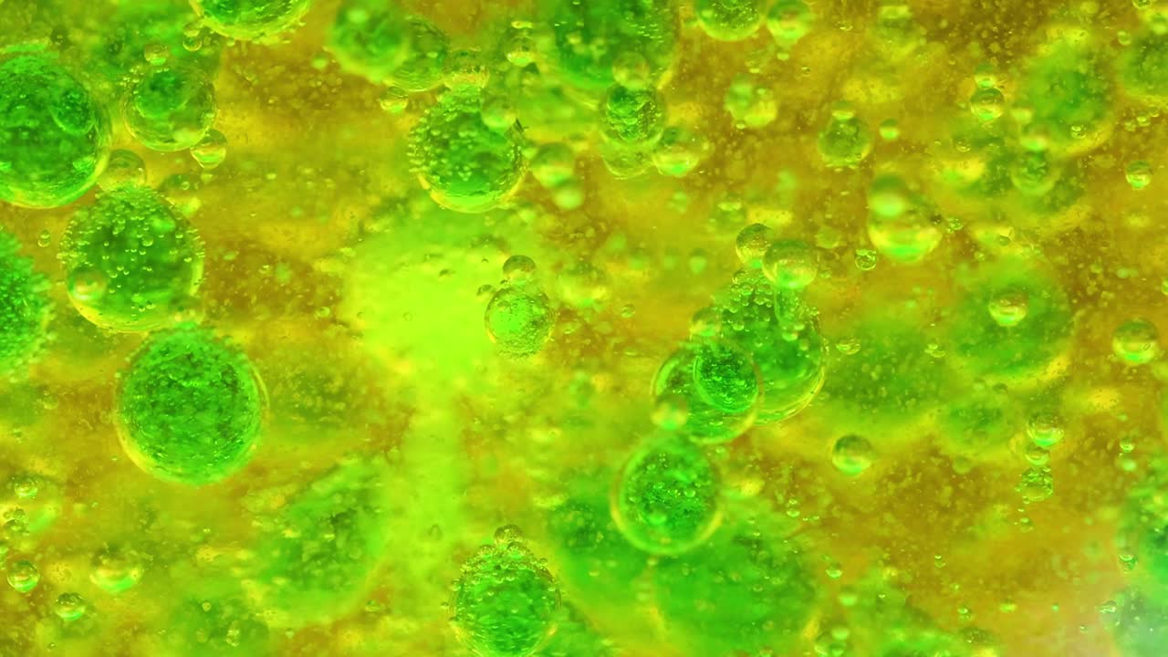 Close-up view of green bubbles suspended in a vibrant yellow liquid, showcasing dynamic patterns and textures.