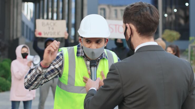 Caucasian journalist or correspondent wearing protective mask in a interview with a builder in a protest against Covid 19