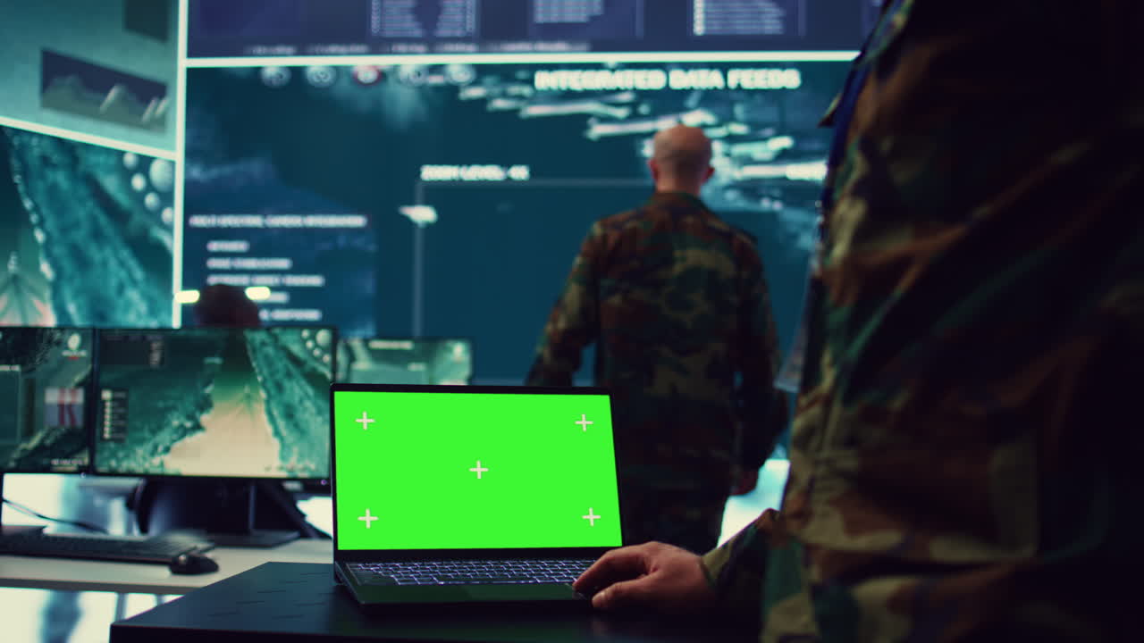 Army officer studies isolated greenscreen display on a laptop in control room