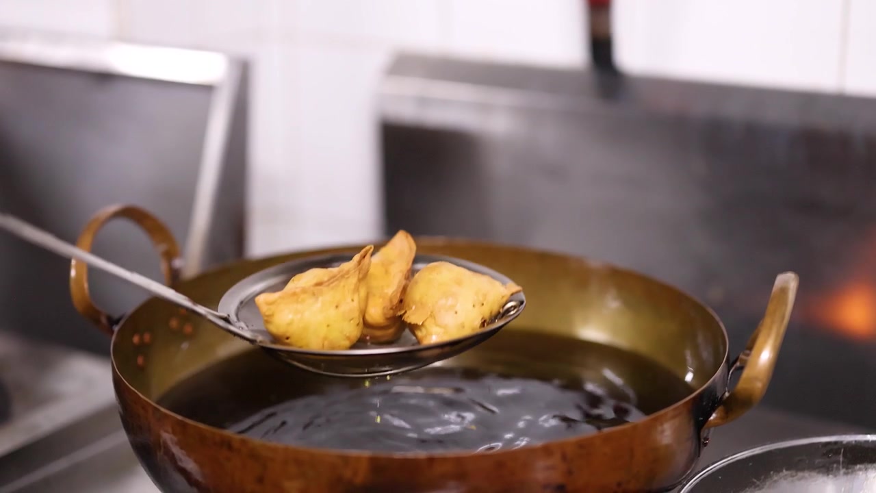 Samosa dorati vengono sollevati dall'olio bollente usando una schiumarola metallica sopra un wok di ottone.