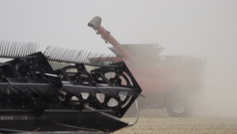 side view of combine harvester collecting grain in dusty farm field