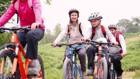 Parents-and-children-riding-mountain-bikes-on-a-path-in-the-countryside-during-a-family-camping-holiday,-Lake-District,-UK