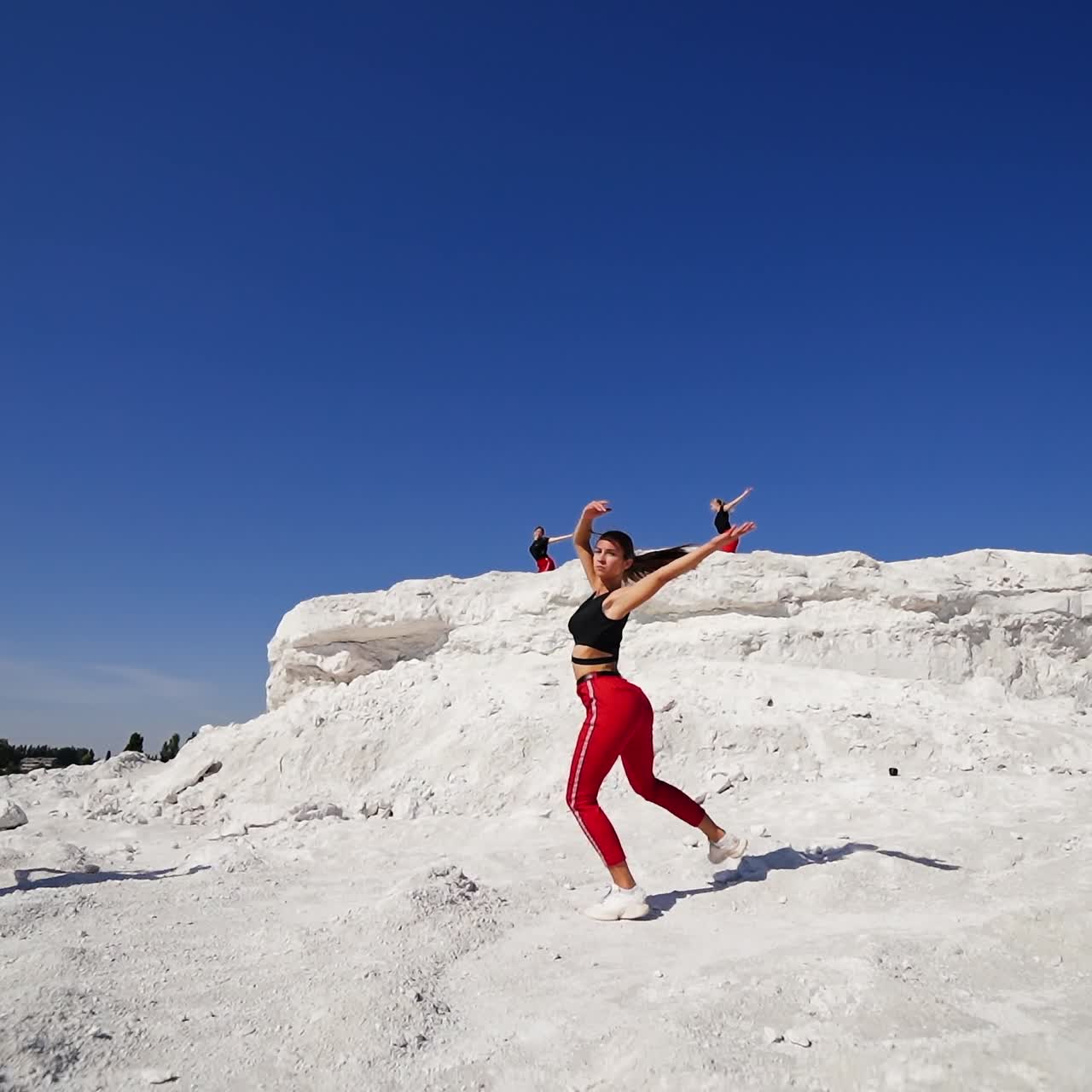 Sportive girls performing stylish group dance outdoors. Collective dancing in the contrasting nature of white rocks and blue skies. Low angle perspective