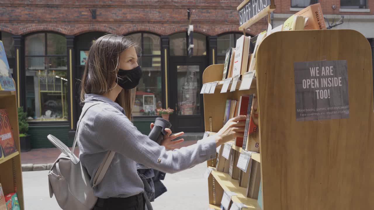 mujer con mascarilla recogiendo libros en un día soleado en una librería al aire libre en portland