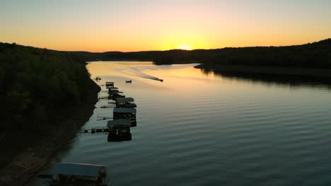 Eine-Drohne-Fliegt-über-Einigen-Bootsanlegestellen-In-Den-Sonnenuntergang,-Während-Darunter-Ein-Vergnügungsboot-Vorbeifährt