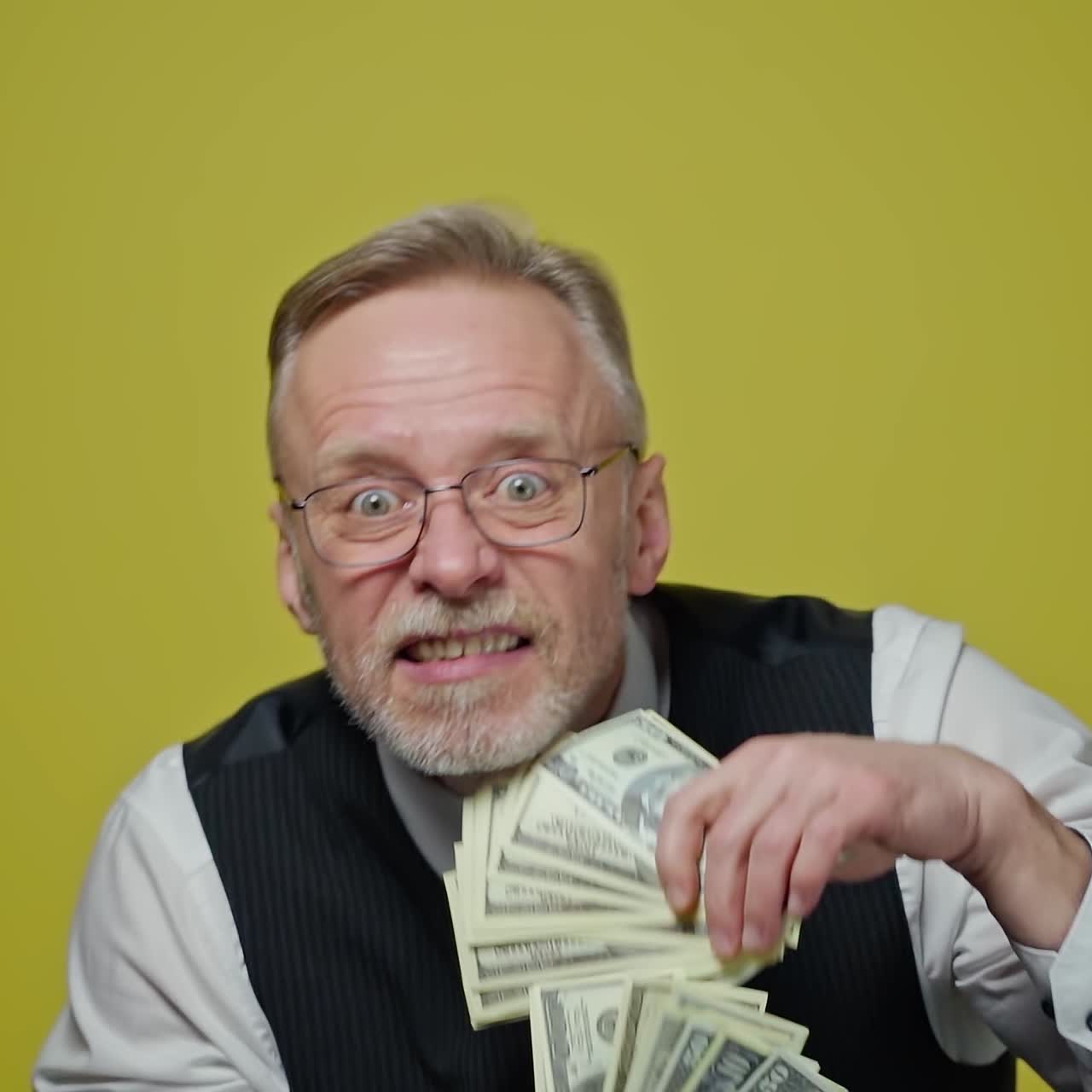 Happy old man with dollars in his hands. Positive rich man demonstrates his money. Face of a funny senior man with money. Close-up.