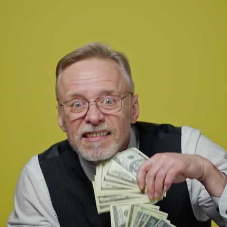 happy old man with dollars in his hands. positive rich man demonstrates his money. face of a funny senior man with money. close-up.