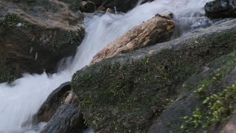 Geringe-Schärfentiefe,-Dolly-Seitenaufnahme-Von-Wasser,-Das-Im-Frühling-Einen-Schnellen-Bach-Mit-Moosbedeckten-Felsen-Hinunterfließt