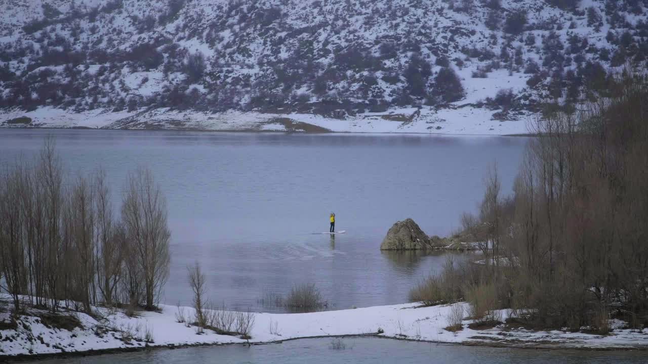 해안의 물과 산 사이에 패들 보드를 탄 남자