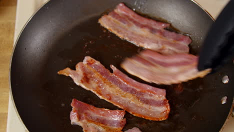 cooking bacon being flipped in a pan