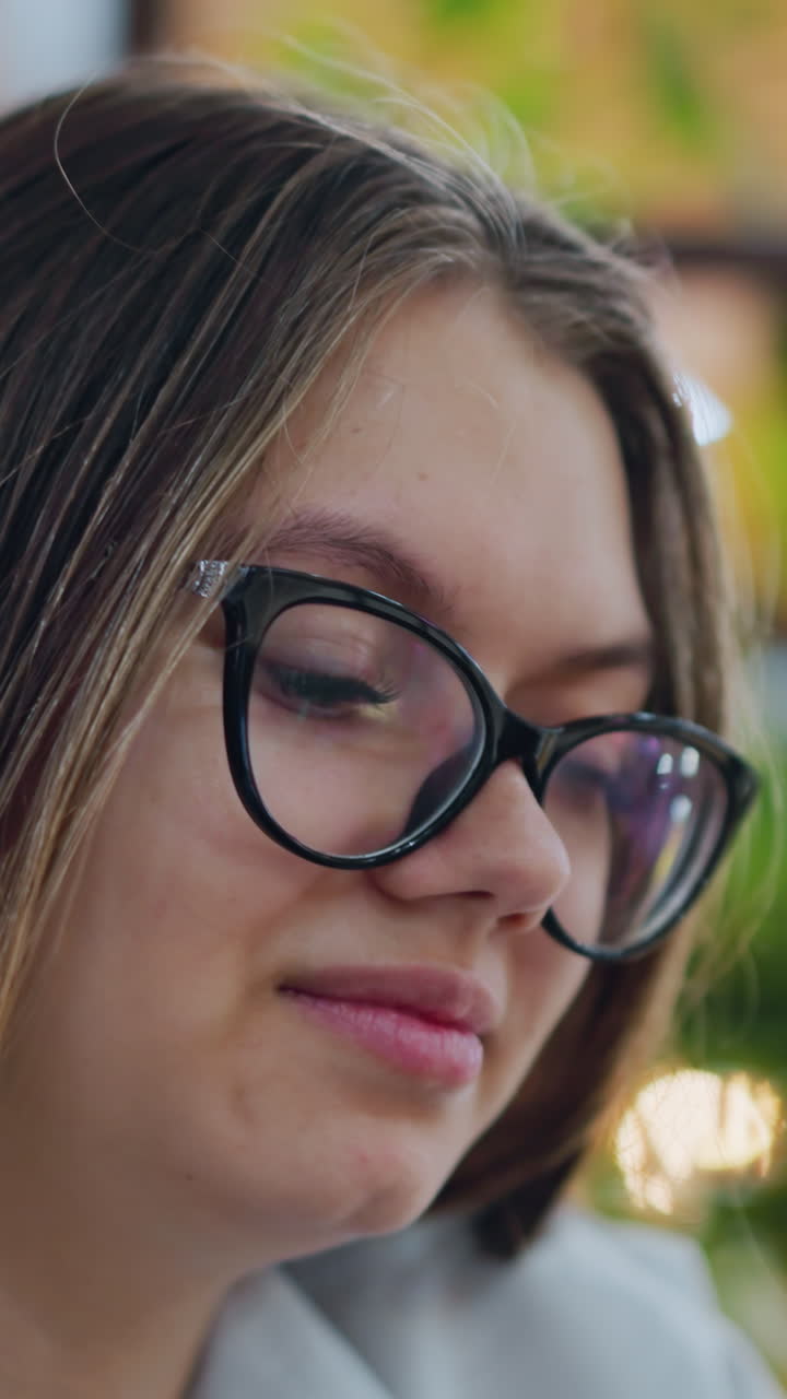 primer plano de una dama elegante con gafas, sonriendo mientras se centra en el teléfono operativo, las cálidas luces bokeh en el fondo mejoran la atmósfera interior moderna y elegante