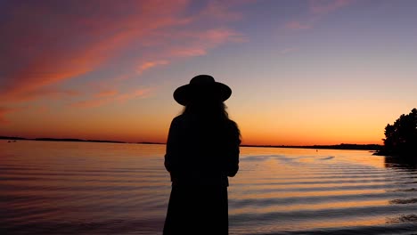 slow motion shot of a young women's silhouette during sunset at the beach with waves slowly crashing into the shoreline at a lake in canada