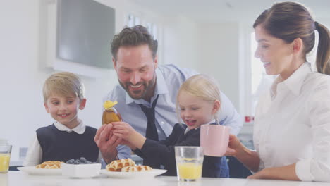 Niños-Con-Uniforme-Escolar-En-La-Cocina-Desayunando-Gofres-Mientras-Los-Padres-Se-Preparan-Para-Trabajar