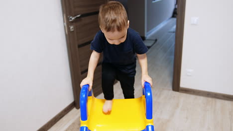 caucasian toddler rises by the stairs of a slide indoors. happy kid taps his feet by the slide and goes down.