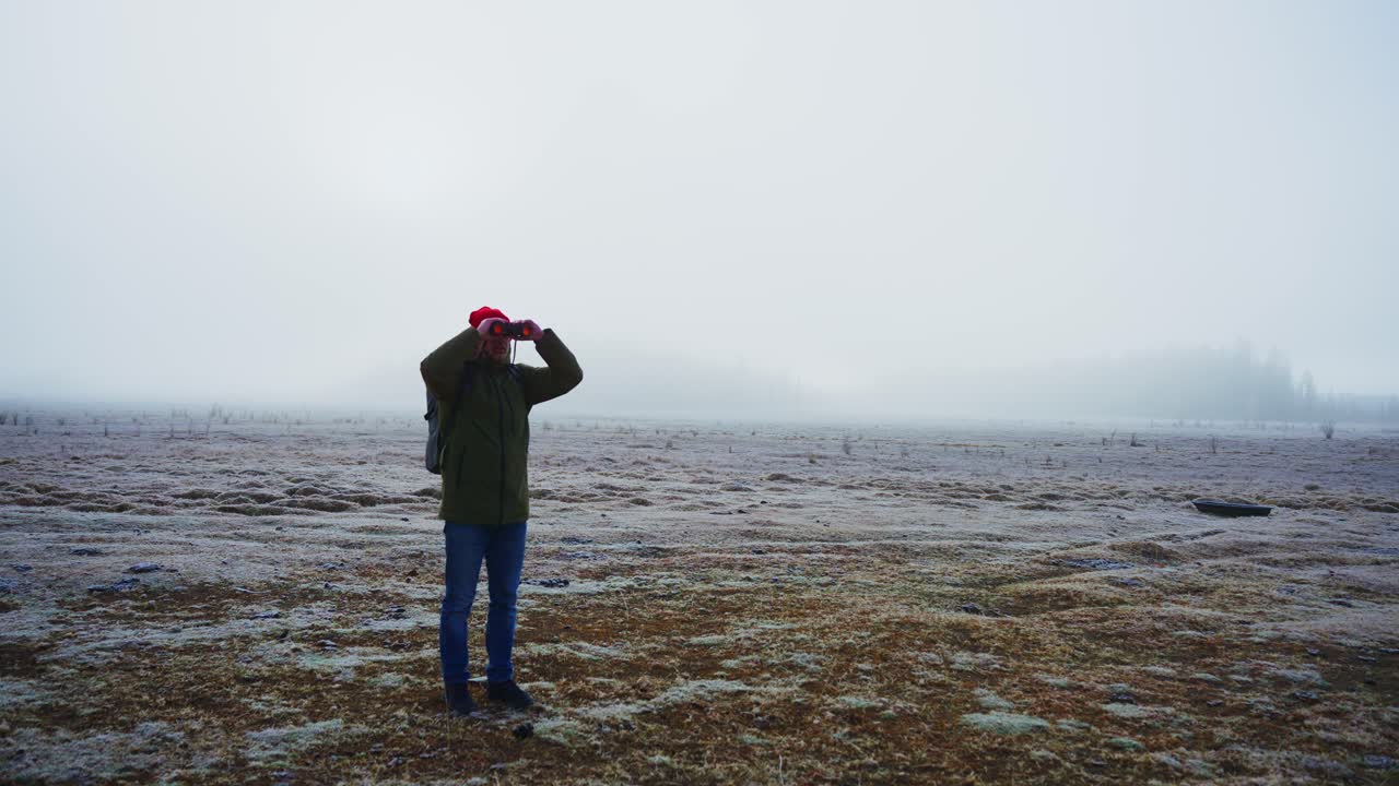 Man using binoculars in a foggy winter landscape