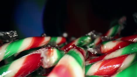 moviéndose a través de la parte superior de una gran pila de mini bastones de caramelo envueltos en rojo, blanco y verde mientras el fondo alterna diferentes colores
