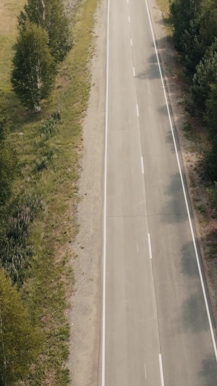 Filmato drone dall'alto di una strada asfaltata a due corsie vuota con segnaletica orizzontale, delimitata da foresta verde e arbusti in una soleggiata giornata estiva, concetto di viaggio e trasporto