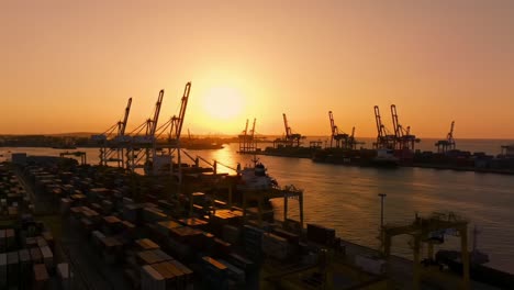 an enchanting sunset over a bustling port: captivating views of cranes, ships, and containers reflecting golden light on calm waters