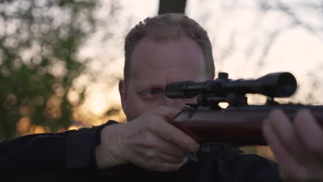 portrait of male hunter aiming his riffle with sunset in the background