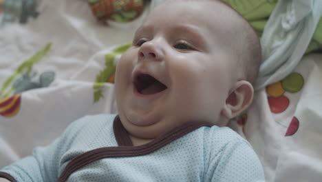 a four months old baby in a happy mood, lies on the coach with colorful bedsheet and looks at his mother