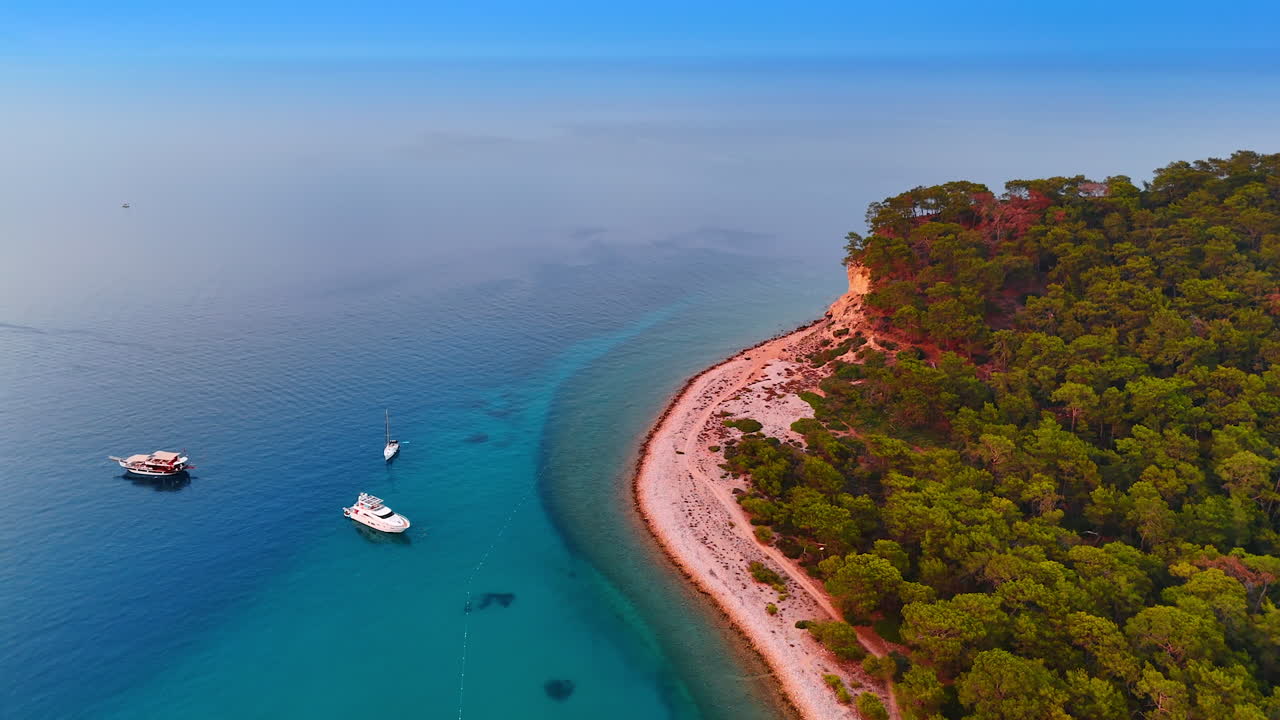 Serene coastal view with boats anchored. Calm waters meet lush greenery along the coastline during a clear day, showcasing the beauty of nature