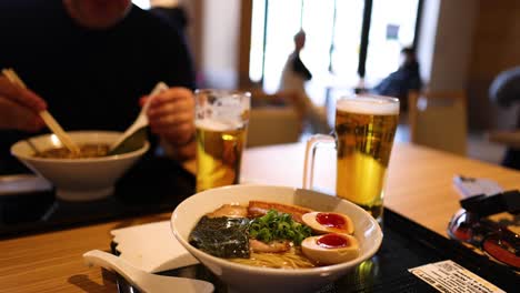 person eating ramen and drinking beer at a table