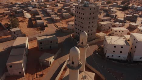 aerial shot of two mosques and a big building in an old empty city in the desert in palestine near gaza at sunset.