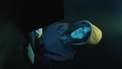 Vertical Shot Of A Woman Wearing Hoodie Jacket, Hacking On A Laptop In Dark Room.