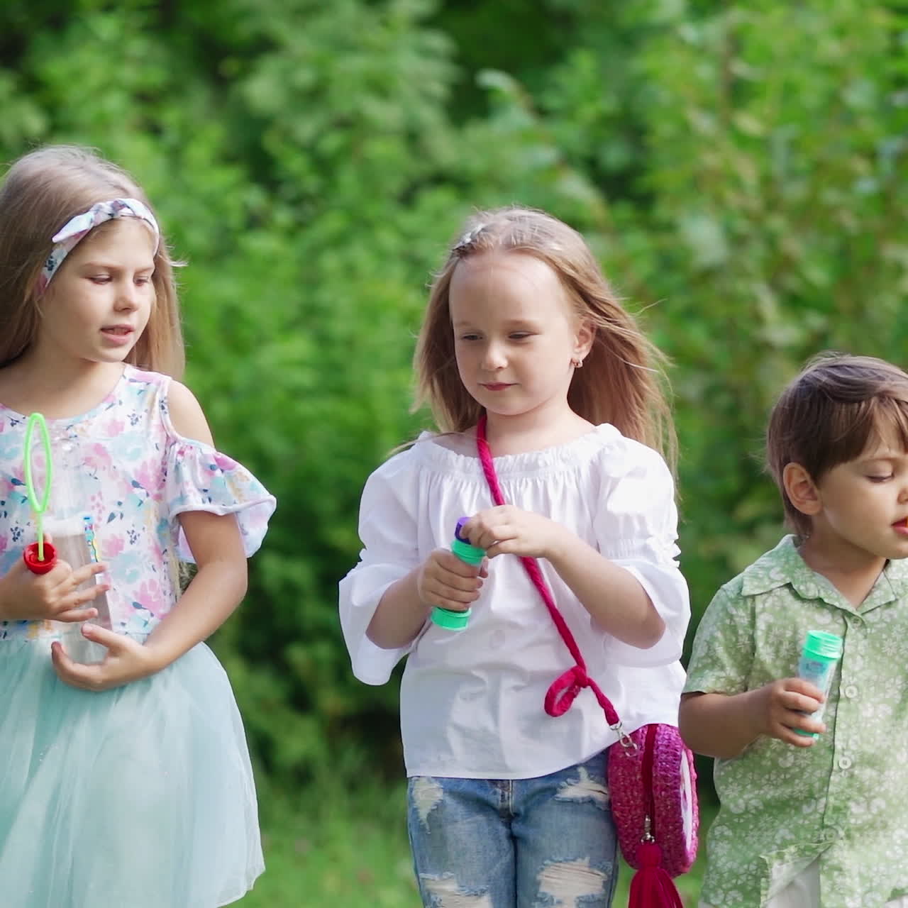 Cute children spending good time in the park. Little girls and a boy blowing soap bubbles outdoors. Happy childhood in summer.