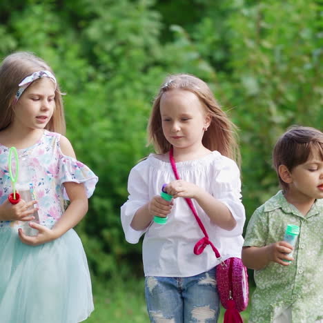 cute children spending good time in the park. little girls and a boy blowing soap bubbles outdoors. happy childhood in summer.