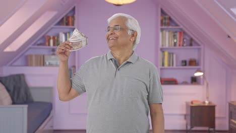 happy indian old man using money as fan