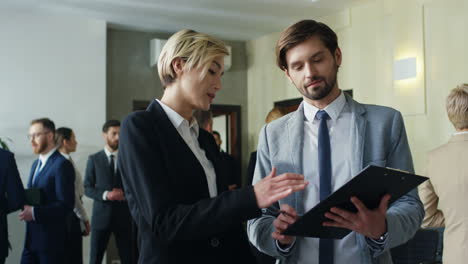 caucasian businesswoman and her male colleague talking and discussing documents in the hall at a meeting