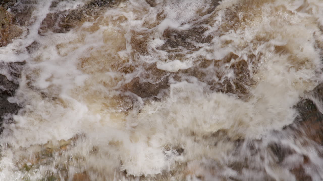 Turbulent stream water churning in chaotic patterns over rocks, expressing untamed energy and the force of nature.