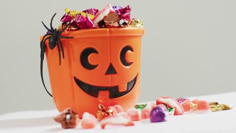 Scary-halloween-pumpkin-printed-bucket-full-of-candies-against-grey-background