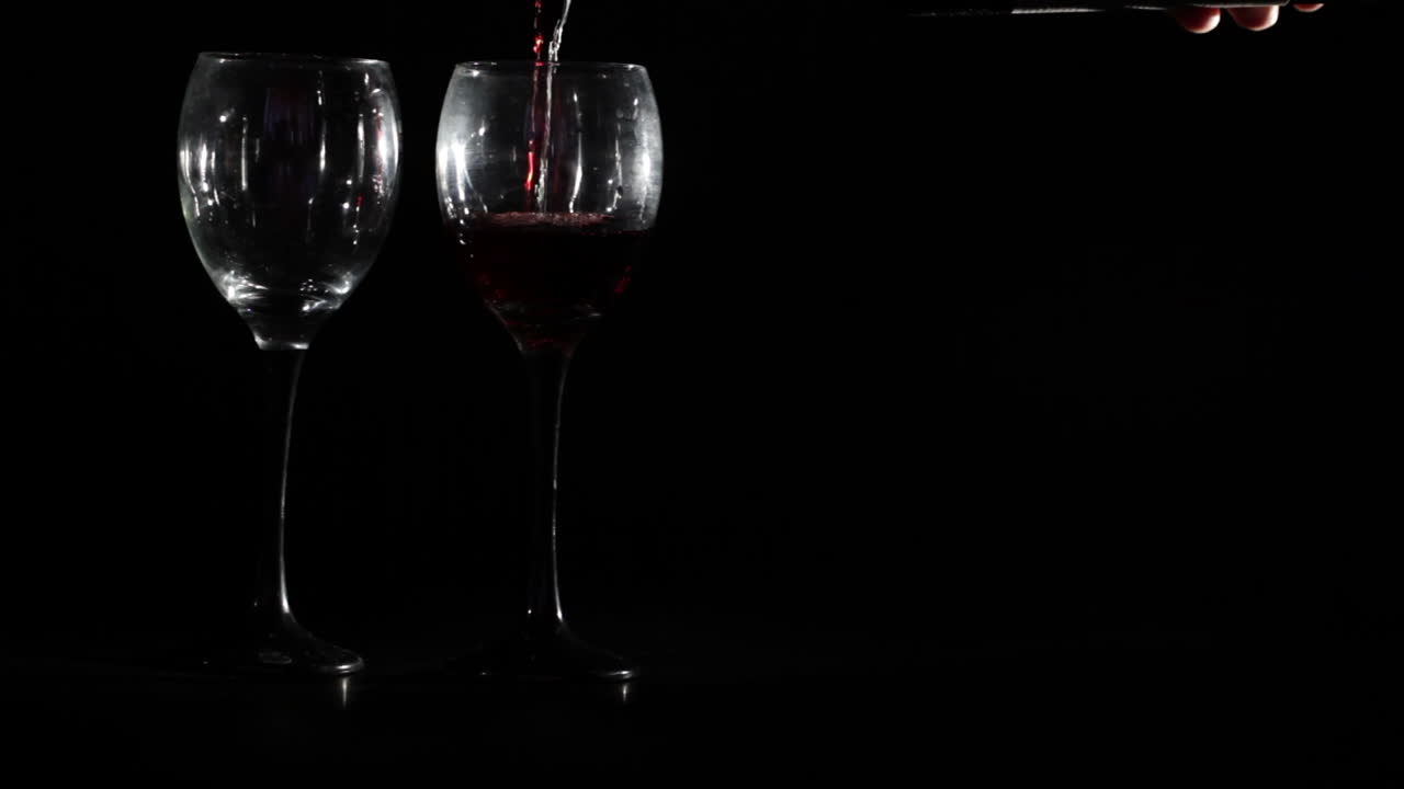 Rødvin hældes i to glas på sort baggrund