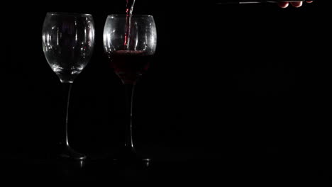 red wine is poured into two glasses on black background