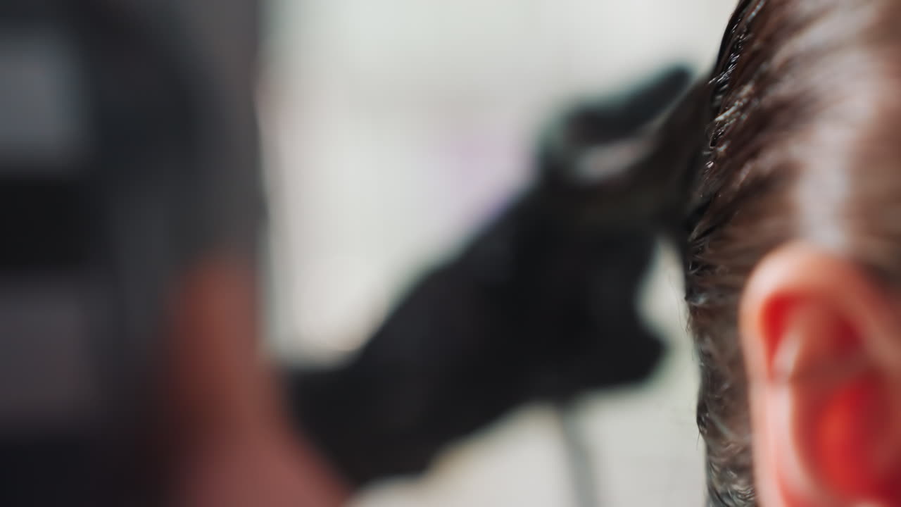 primer plano de una técnica de coloración de la raíz del cabello, escena de un salón moderno con una estilista que colorea cuidadosamente las raíces del cabello, coloración precisa del cabello mientras la estilista separa el cabello con guantes y un pincel en el salón