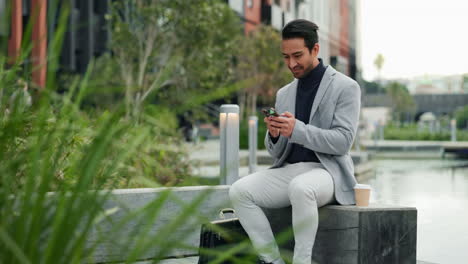 a businessman sits on a bench outside a city building, smiling and looking at his phone.