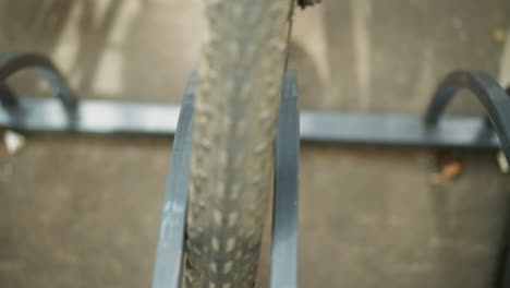 primer plano de un neumático de bicicleta trasladado a un soporte de bicicleta de metal, enfatizando la rueda, el marco y los rayos con una vista detallada contra el pavimento de alquitrán de carbón y las sombras suaves en el hormigón