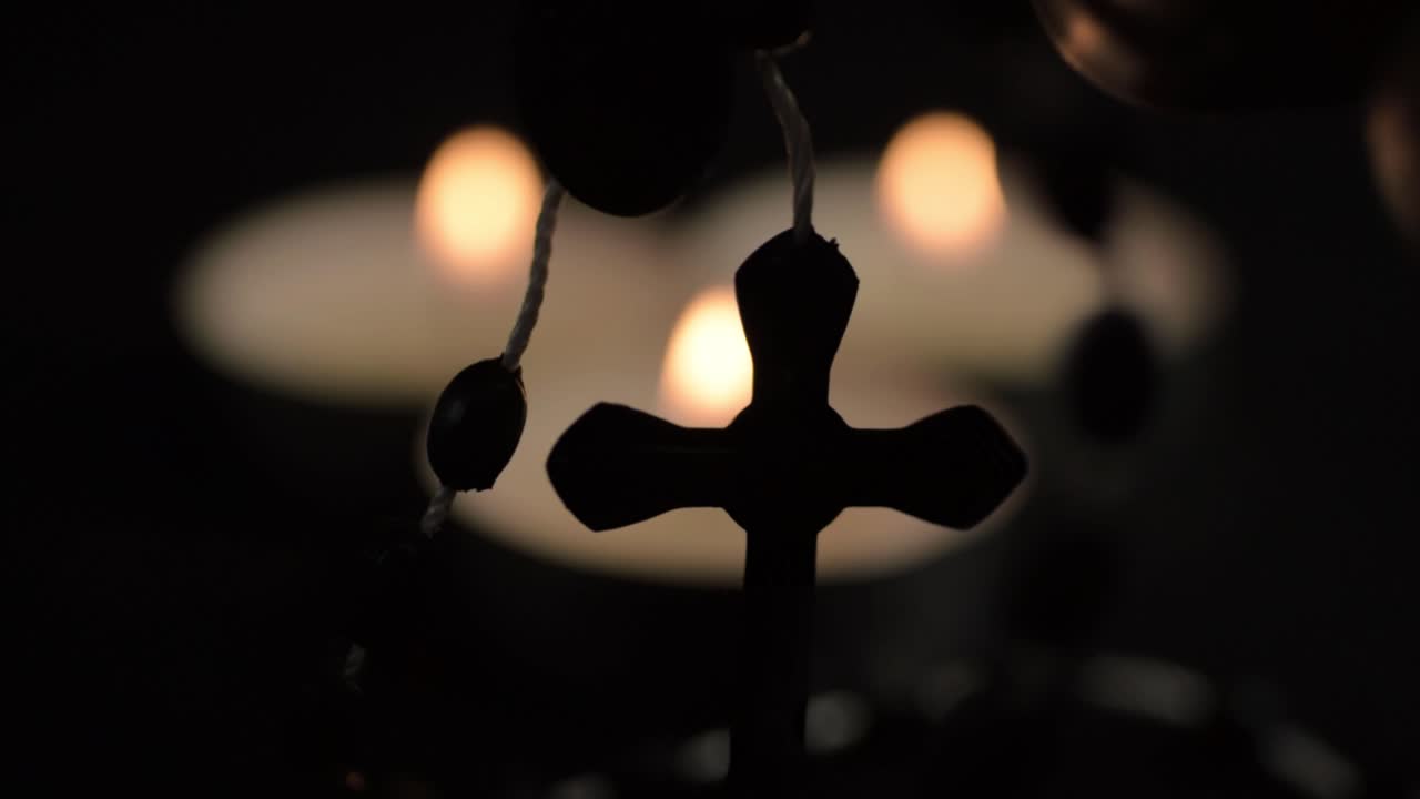 Holding rosary beads with bokeh of tea light candles background close up