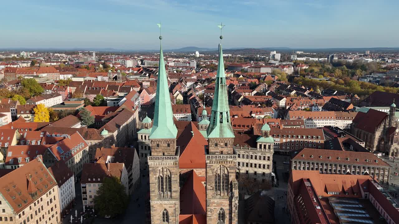 Drone flies toward the twin spires from a frontal angle with the old town grid stretching into the distance
