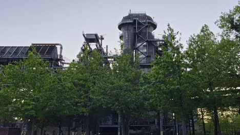 old industrial structures and buildings jut out between trees in the setting sun in the landschaftspark in duisburg nord in germany