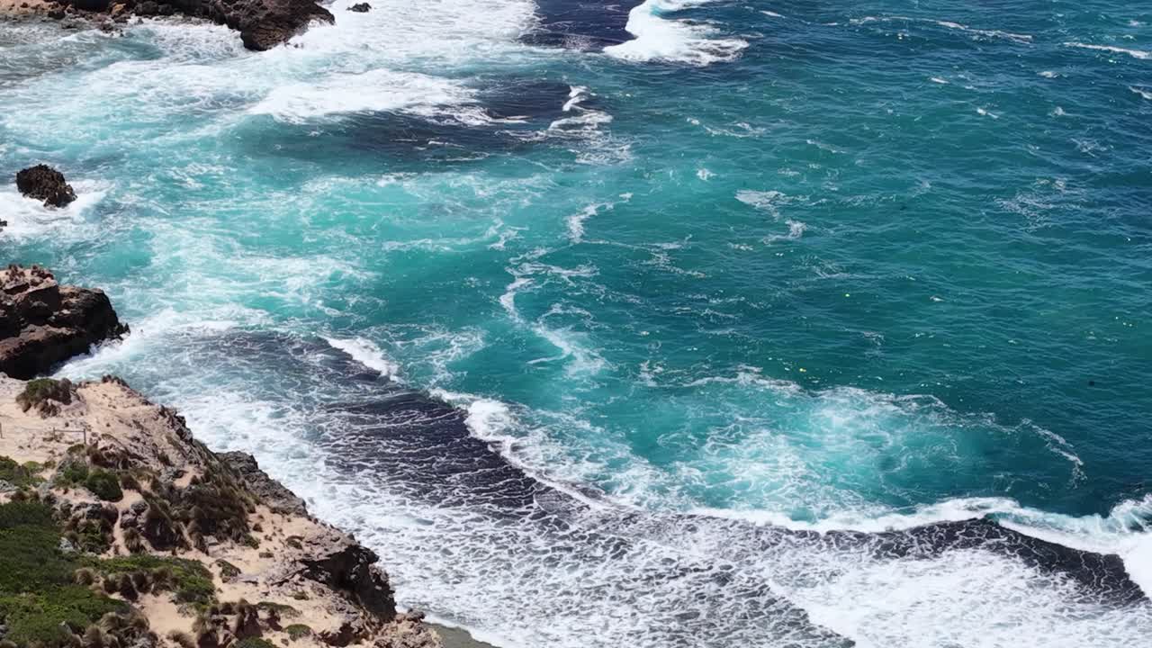 Uma fotografia aérea em um ângulo alto feita por drone captura ondas turquesa quebrando contra a costa rochosa e acidentada da Península de Mornington