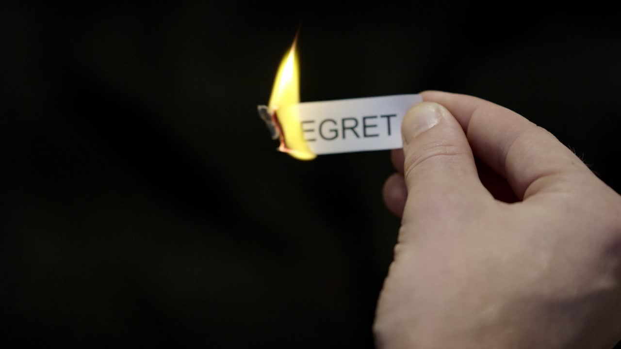 Queimando o Arrependimento - Mão Incendiando Nota de Papel Marcada como “ARREPENDIMENTO”, Poderosa Liberação de Críticas, Culpa e Vergonha, Close-up Cinematográfico Escuro. Saúde mental, terapia.